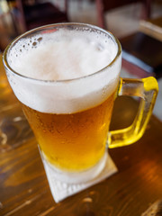 Closeup vertical detail of a beer stein containing ice cold lager with a foamy head. Shallow focus. Bangkok, Thailand. Travel and party.