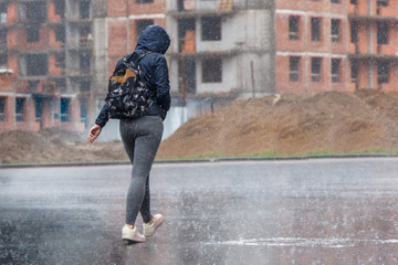 a woman with a backpack and a hood runs in the pouring rain