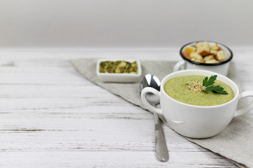 Vegetarian cream of broccoli, potato, onion, garlic, sesame and olive oil, and coconut milk .soup served in a white ceramic plate on a light wooden background using light textile