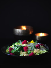 Obraz premium Delicious and colorful green salad with raspberries on dark background in quiet environment