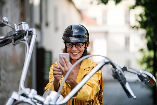 Cheerful senior woman traveller with motorbike in town, taking selfie.