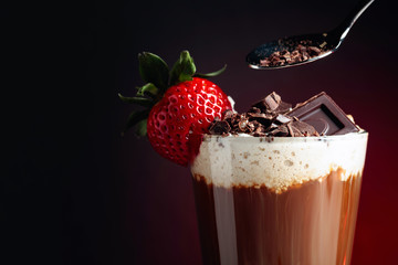 Coffee drink with whipped cream, strawberry and pieces of black chocolate on a dark background.