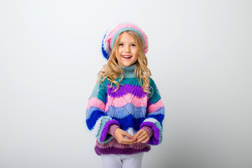 little blonde girl smiling in knitted hat and sweater on white background isolate, space for text