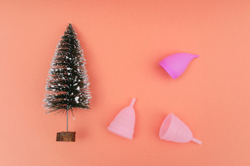 Pink menstrual cups and christmas tree on color background, female intimate hygiene period products, top view. Holiday concept