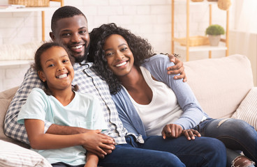 Loving afro family cuddling and smiling to camera at home