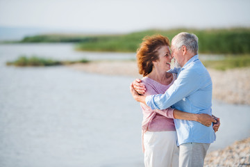 Senior couple on a holiday on a walk by the lake, hugging. Copy space.