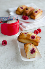 Financier cakes with raspberry and coconut flakes on white plate on light background