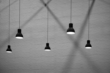 Side view and selective focus of 5 hanging lamps with light and shadow on surface of brick wall...