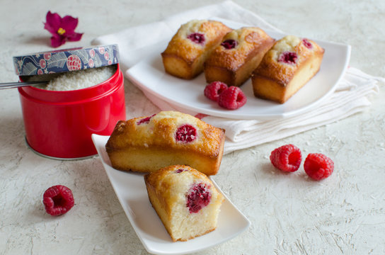 Financier cakes with raspberry and coconut flakes on white plate on light background
