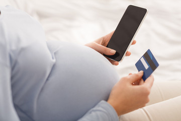 Pregnant woman shopping online using smartphone and credit card