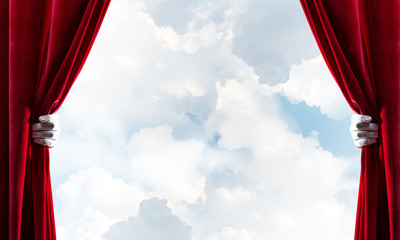 Cloudy landscape behind red curtain and hand holding it