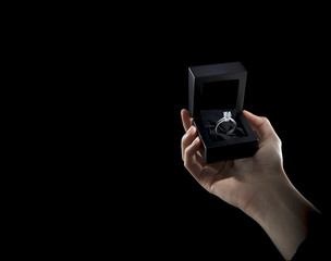Hand holding diamond ring in black box, with black background