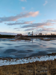 The river covered with thin ice glows from the sun. On the other side is a small white church