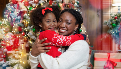 Portrait of happy black mother and daughter posing near Christmas tree