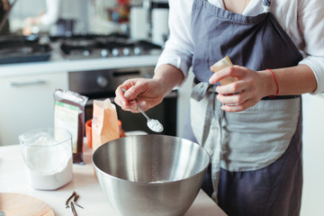 Crop woman pastry chef or baker preparing a cake and puts flour in a bowl.