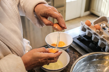 Hands of mature woman in bathrobe separating eggs on island in kitchen - Selective focus