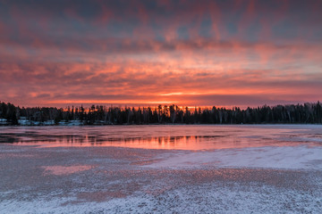 A fiery sunrise reflects off of the ice of a frozen lake in Northwest Ontario, Canada.