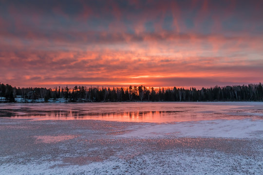 A fiery sunrise reflects off of the ice of a frozen lake in Northwest Ontario, Canada.
