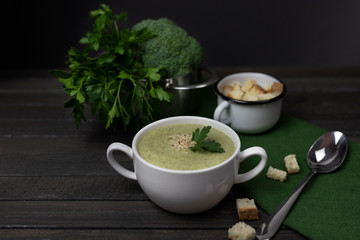 Vegetarian cream of broccoli, potato, onion, garlic, sesame and olive oil, and coconut milk soup. served in a white ceramic plate on a dark brown wooden board using green textile