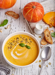 Bowl of pumpkin and carrot cream soup with seeds and basil leaf. Vegetarian homemade dish