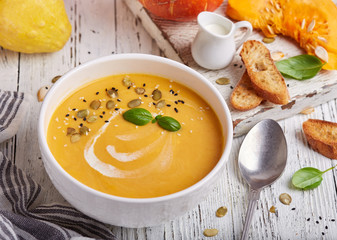 Bowl of pumpkin and carrot cream soup with seeds and basil leaf. Vegetarian homemade dish