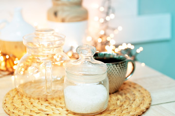 Christmas mood in the kitchen with lights and bokeh. A cup with a jar of sugar on a wicker stand.