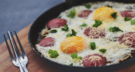 fried egg with ham sausage and cheese in a frying pan on wooden table background
