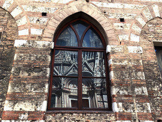 Reflection of the Siena Cathedral in a window on the old wall at the Piazza del Dumo