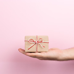 Male hand on a pink background holding craft gift. Christmas concept symbol, commercial bucket print, copy space.