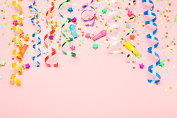 Colorful ribbons with paper stars and confetti on pink background
