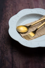 Empty plate with brass spoon and fork on wooden background