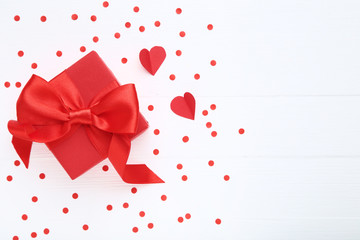 Gift box with ribbon bow and paper hearts on white wooden table