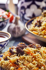 Uzbek pilaf in an authentic blue and gold dish, shot on a blue background with tomatoes, garlic and tea