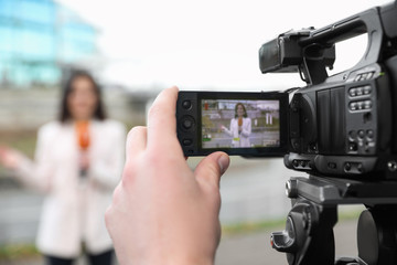 Young male journalist and video operator working on city street, focus on camera display