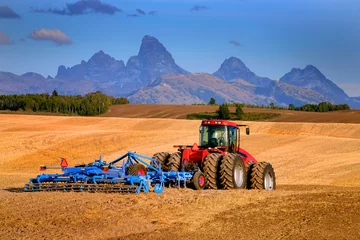 Gordijnen Tractor Farming Ground Harvesting Crops in Fall Autumn Teton Mountains Rugged © Lane Erickson