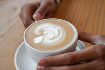 Tasty cappuccino in white cup in street cafeteria on wooden table, female hands holding cup, person having relax and time for dreaming, coffee in great afternoon energy idea, closeup image