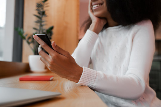 Cropped image of beautiful black woman sitting alone and holding mobile Smart Phone in hand, smiling and looking happy. 