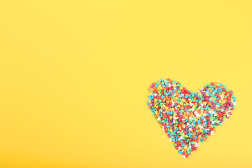 Colorful heart shaped sprinkles on yellow background