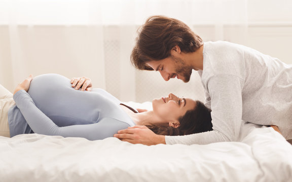 Young pregnant woman enjoying spending time with her husband in bed