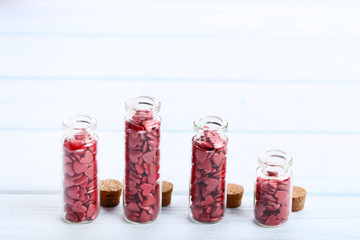 Red heart shaped sprinkles in glass bottles on wooden table
