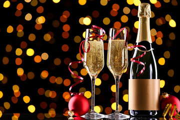 Bottle and glasses of champagne with red baubles on blurred lights background