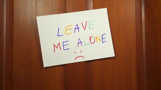 Tilt up to a hand written LEAVE ME ALONE sign on a door. Trying to get away from it all to find privacy and solitude.