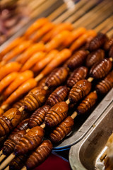 Grill and fried silkworm pupae in a food market in Beijing, China.