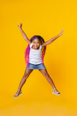 Cute little afro girl jumping over yellow studio background