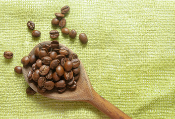 Wooden spoon with brown coffee beans. On the green cloth. Roasted coffee.  Grow your coffee.