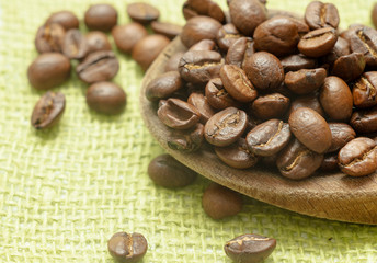 Wooden spoon with brown coffee beans. On the green cloth. Roasted coffee.  Grow your coffee.