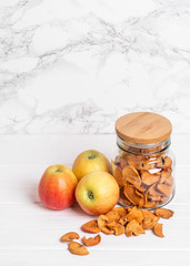 Dried apples in a glass jar with a wooden lid with fresh apples on a light background