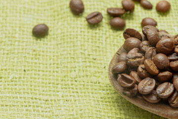 Wooden spoon with brown coffee beans. On the green cloth. Roasted coffee.  Grow your coffee.