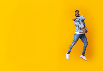 Fototapeta na wymiar Funny jumping black guy pointing at copy space on yellow background