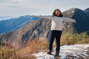 A little girl on the edge of a snow covered mountain, expressing joy after reaching the hiking...